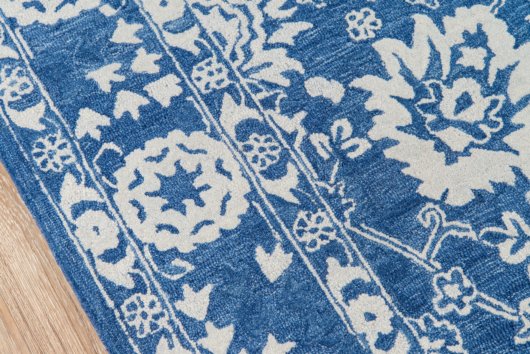 Blue and white floral patterned rug with decorative borders on a wooden floor.