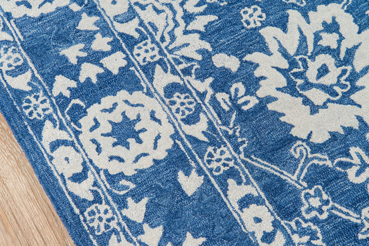 Blue and white floral patterned rug with decorative borders on a wooden floor.