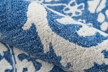 Blue and white patterned rug with plush tufted pile, rolled edge revealing a floral-inspired motif.
