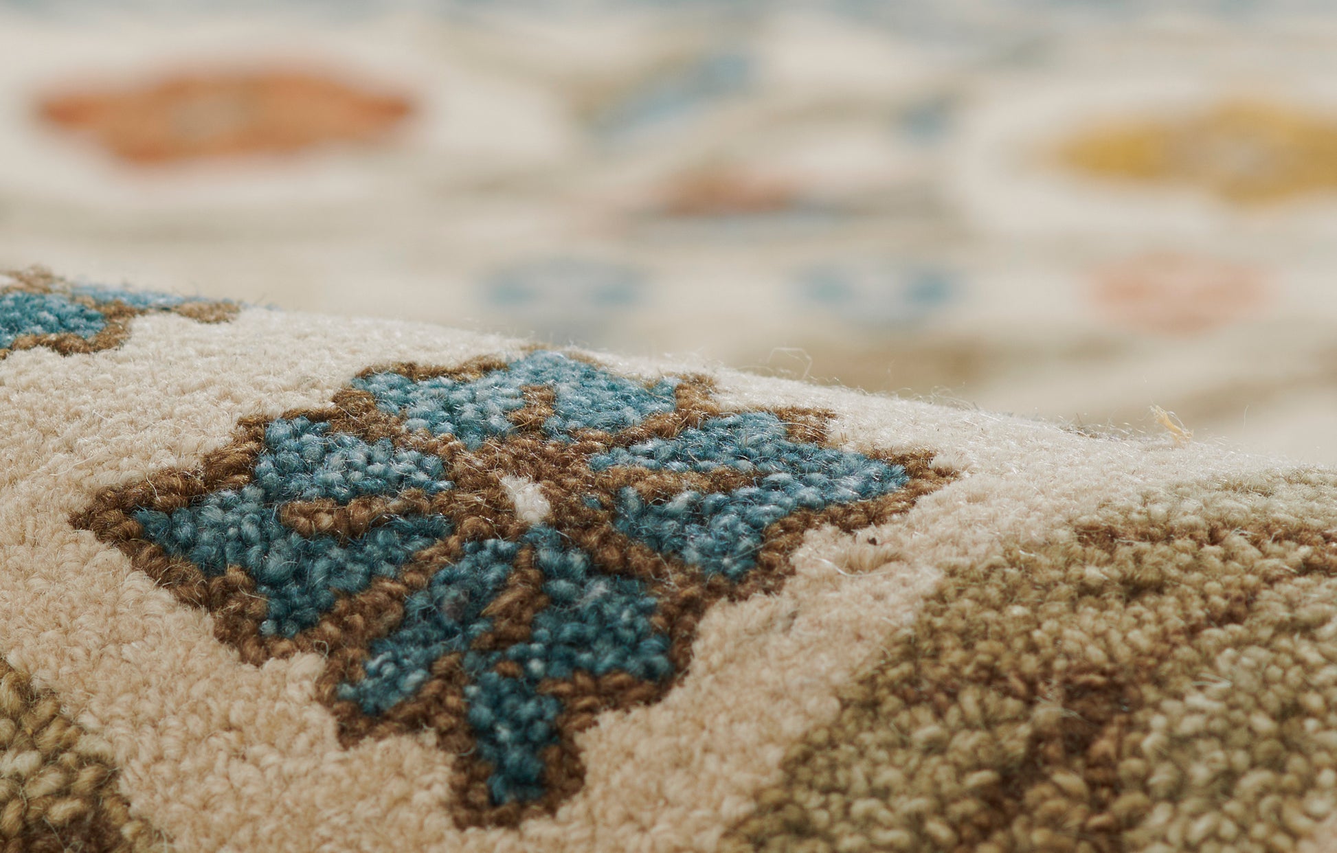 Close-up of a beige woven rug with blue teal floral motif and brown outlining; soft wool pile for living room decor.