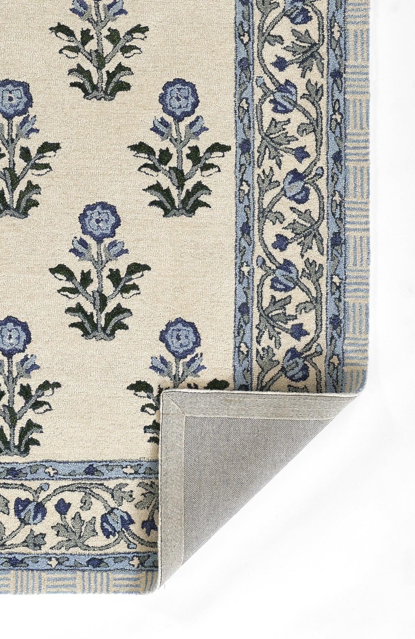 Beige woven rug with blue floral motifs and ornate border; folded corner shows backing.