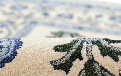 Close-up of a beige rug with blue floral designs and green accents in a plush tufted pile.