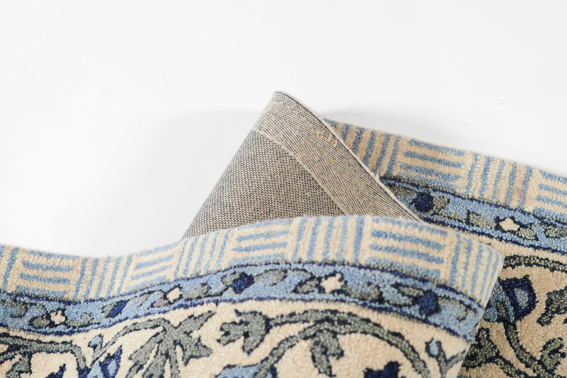 Blue and cream woven rug with ornate floral border, folded corner revealing light beige underside.