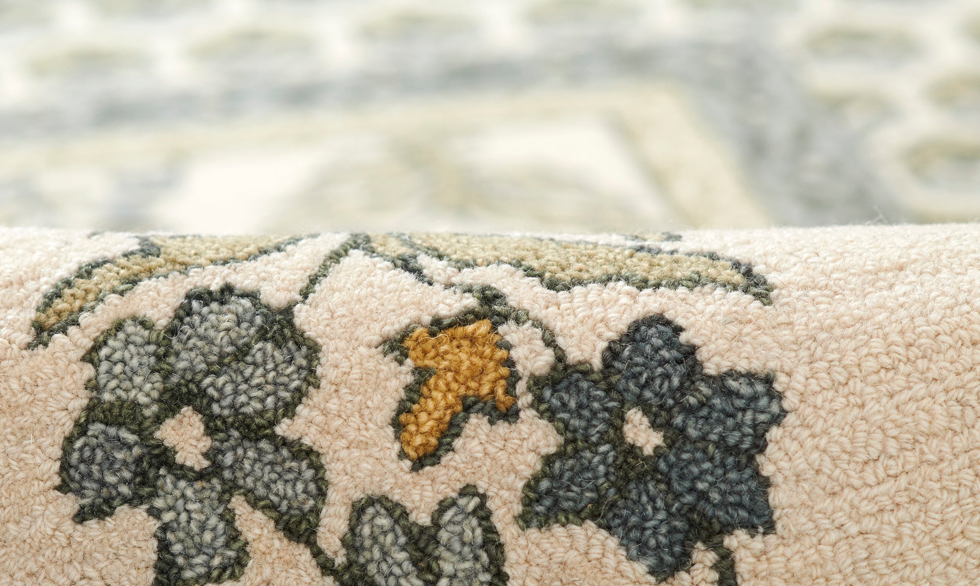 Close-up of a cream woven rug edge with dark blue flowers, gray leaves & a mustard-yellow leaf accent.