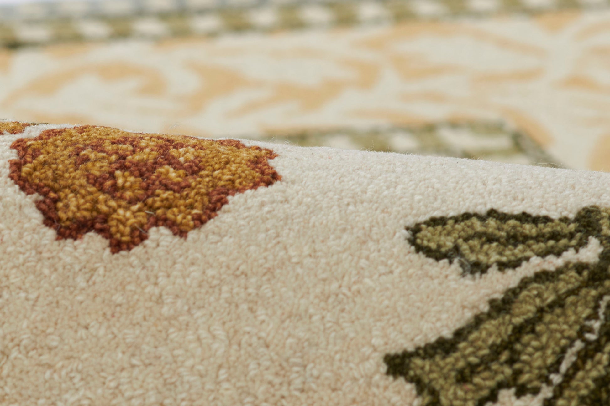 Close-up of a beige woven rug with orange-gold and dark-green floral motifs and textured pile.