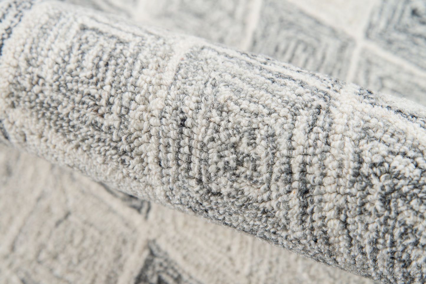 Rolled gray geometric rug with raised loop-pile texture for contemporary living spaces.