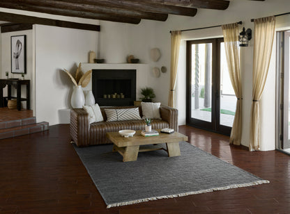 Rustic living room with brown leather sofa, wooden coffee table, gray rug, white walls, exposed beams, and French doors.