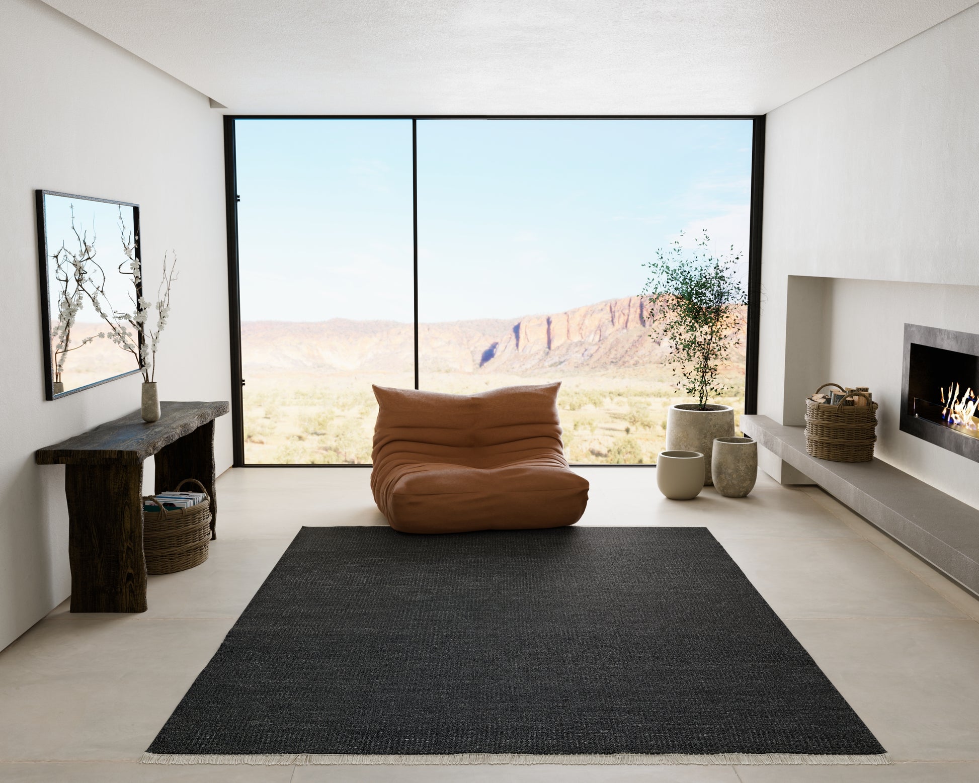 Minimalist living room with floor-to-ceiling desert view, brown bean bag, dark rug, fireplace, and potted plants.