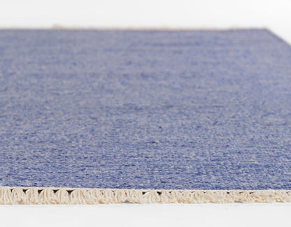 Blue textured rug with beige fringe along the edge, close-up view of pile and weave.