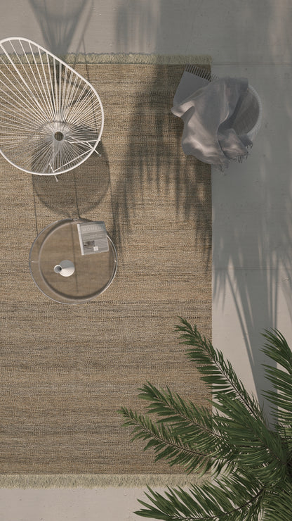 Overhead view of a beige outdoor rug with a white circular wire chair, round glass table, gray accents, and palm fronds.