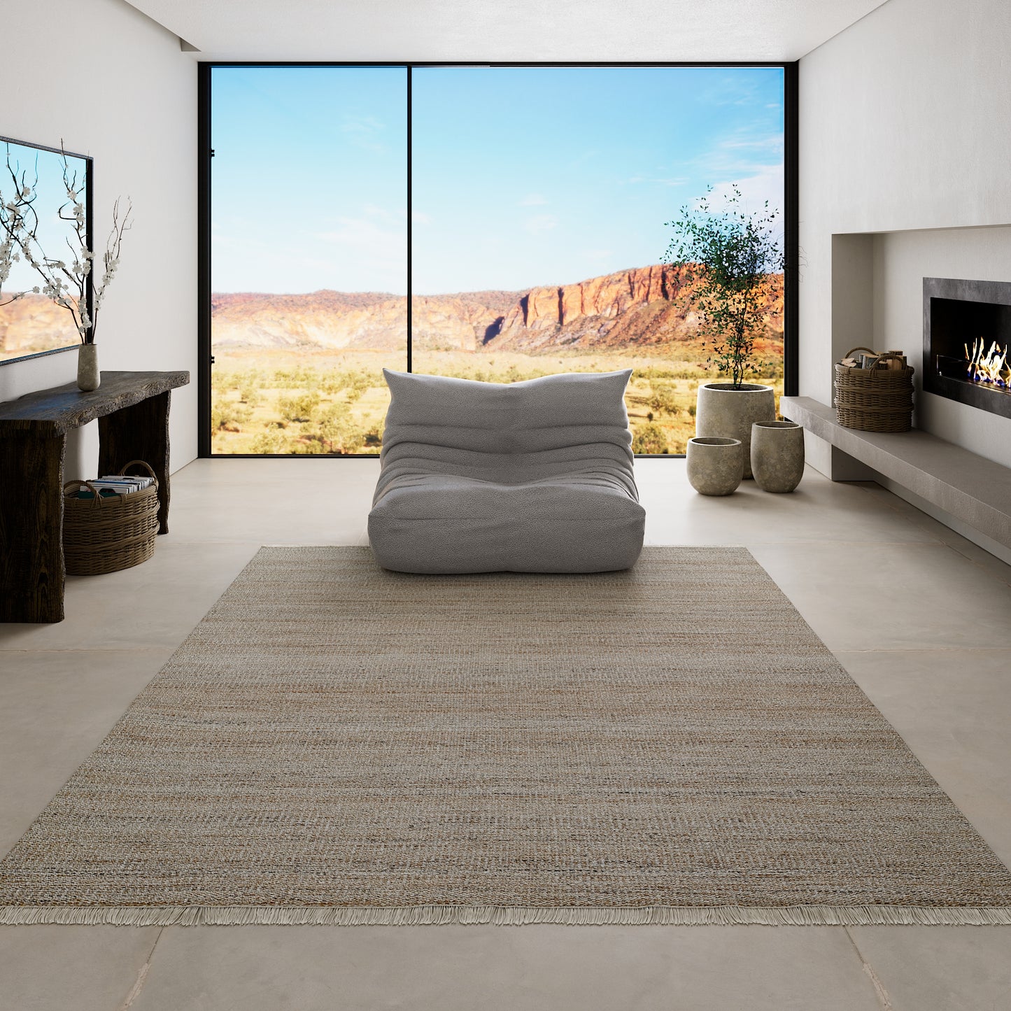 Soft gray fabric floor cushion in a minimalist living room with desert landscape view, tan rug, and modern fireplace.