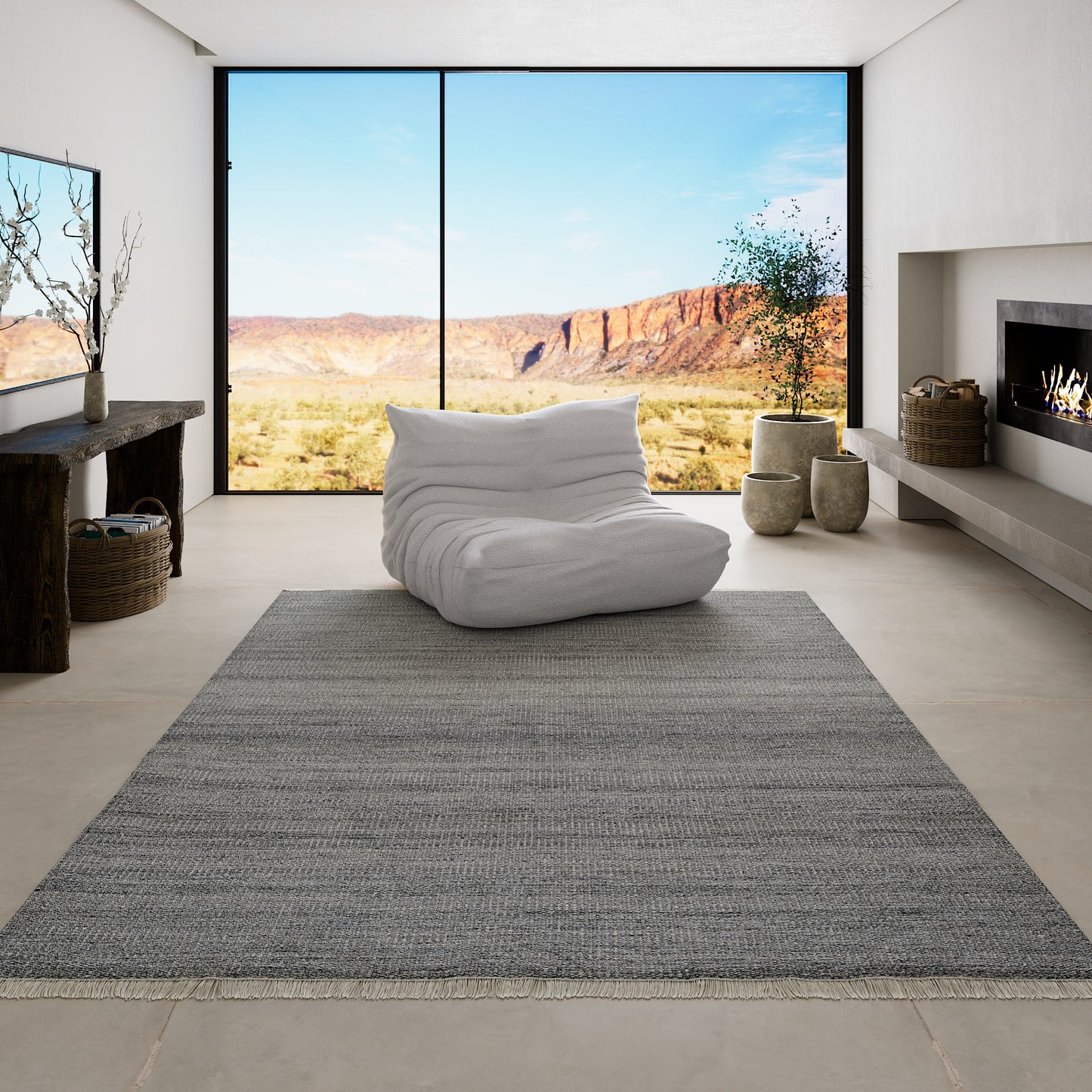 Minimalist living room with large desert canyon view through window; white bean bag on gray rug, fireplace, potted plants.