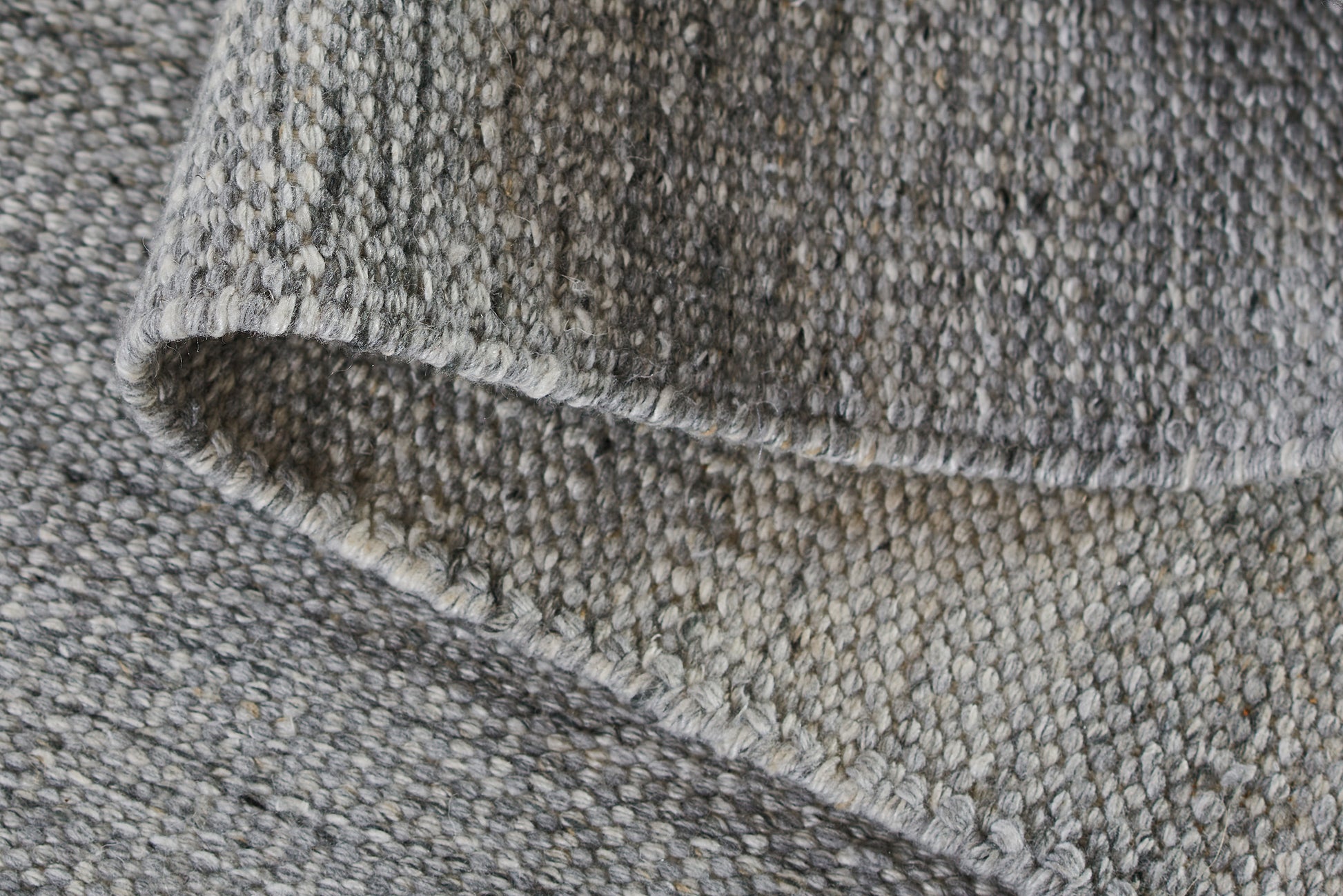 Close-up of a grey heather rug with a knit-like texture, chunky stitches and a folded edge; size 10' x 14'.