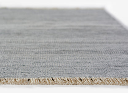 Gray-blue flat-weave rug with natural beige fringe edge, casual coastal living room decor.