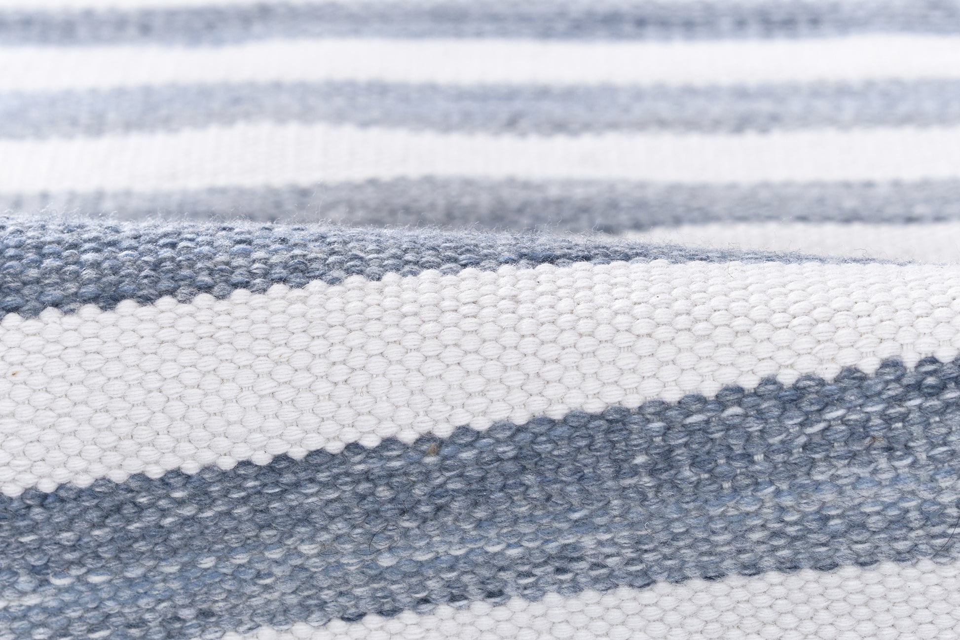 Close-up of blue and white striped woven rug with a textured surface, casual coastal-style.