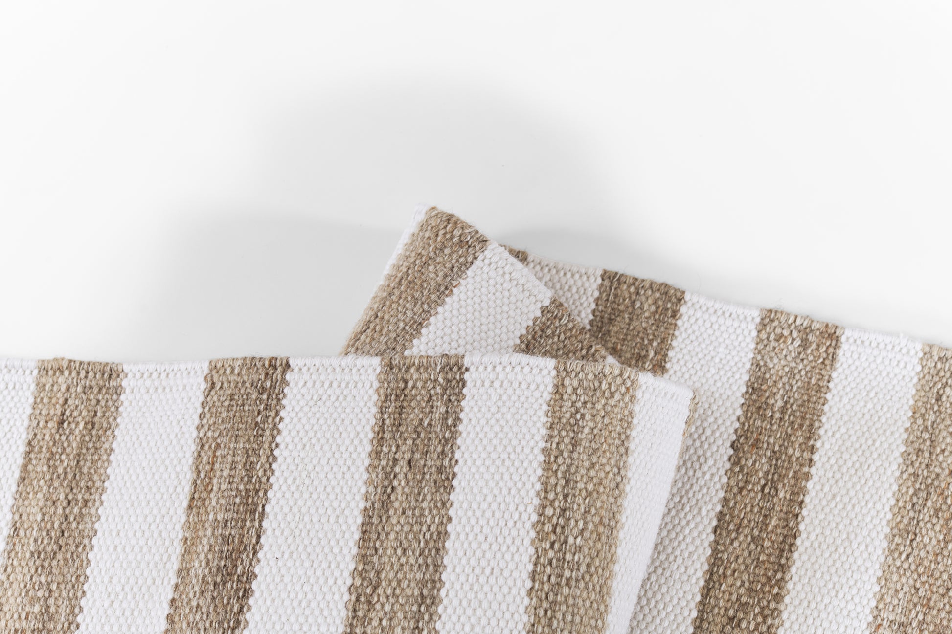 Beige and white striped rug with a woven cotton texture, folded in overlapping pieces.