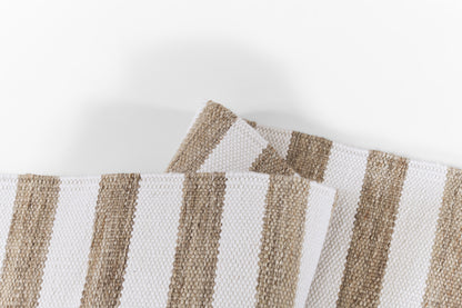 Beige and white striped rug with a woven cotton texture, folded in overlapping pieces.