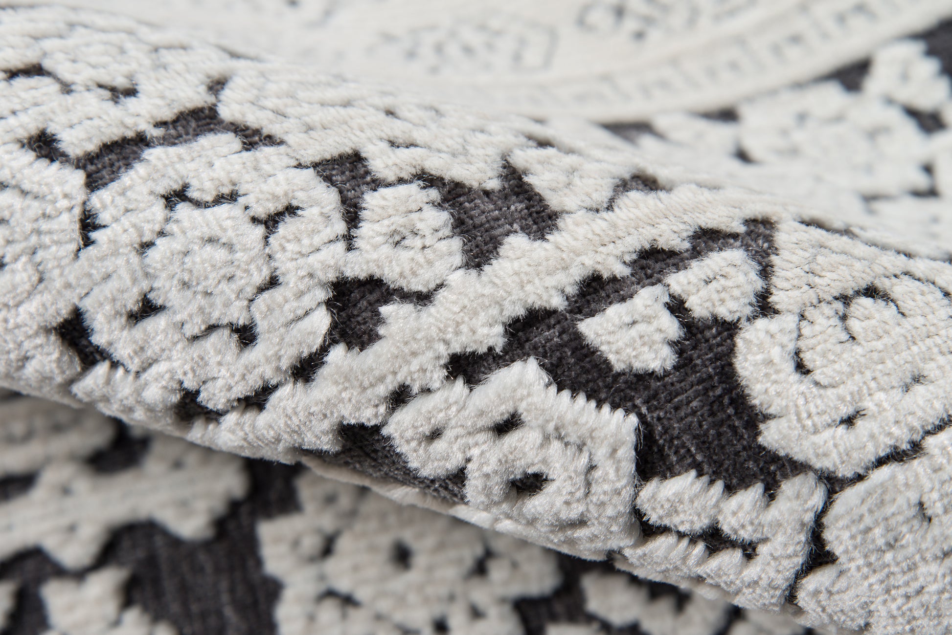 Close-up of cream and charcoal damask floral rug with a textured woven pile.