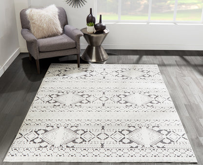 Light gray geometric rug with diamond pattern on dark wood floor, gray chair with cream fluffy pillow and metal side table.