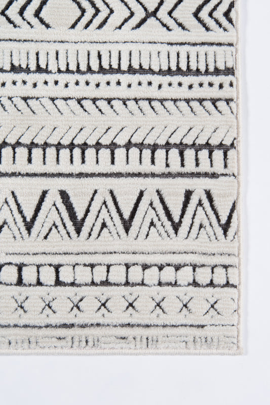 Close-up of a black and ivory geometric woven rug with chevrons, stripes, and fringe along the edge.