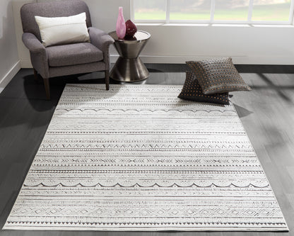 Rectangular light grey rug with black geometric patterns on dark wood floor, living room with grey chair and pink vases.