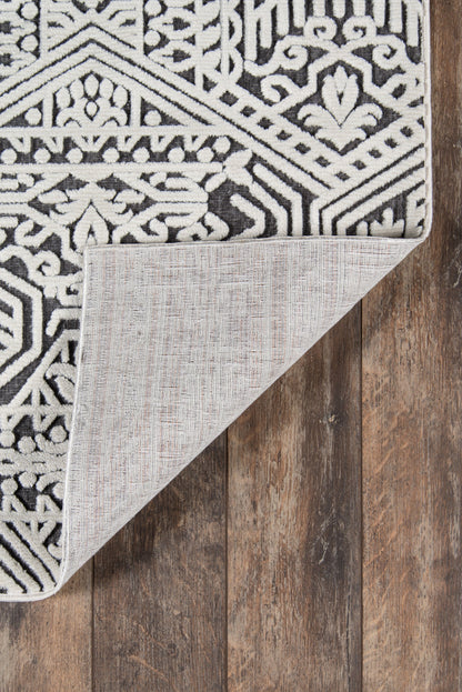 Rectangular black-and-white geometric rug, folded corner reveals light grey backing on wooden floor.