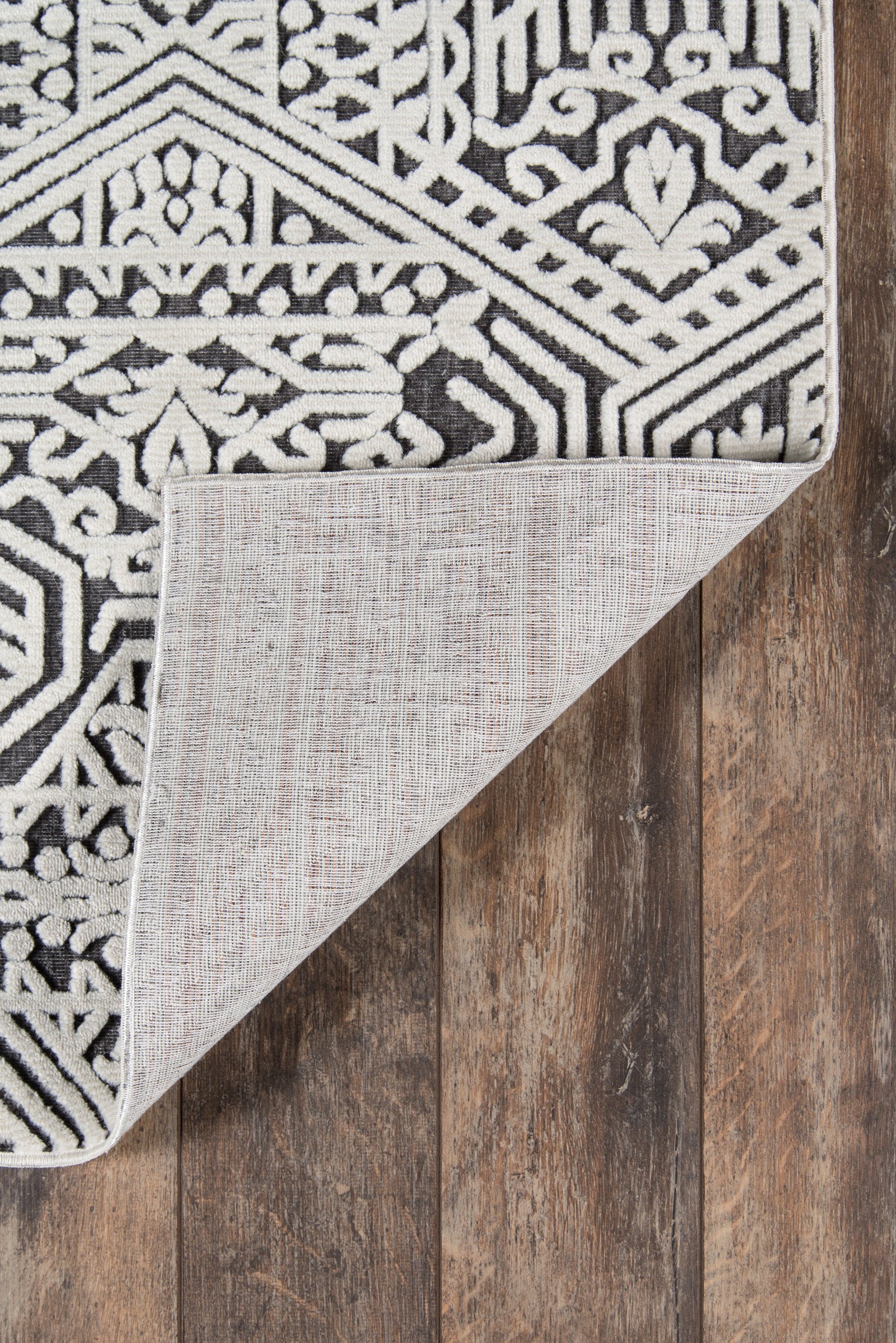 Black and white geometric rug on wood floor; folded corner reveals light gray backing and woven texture.