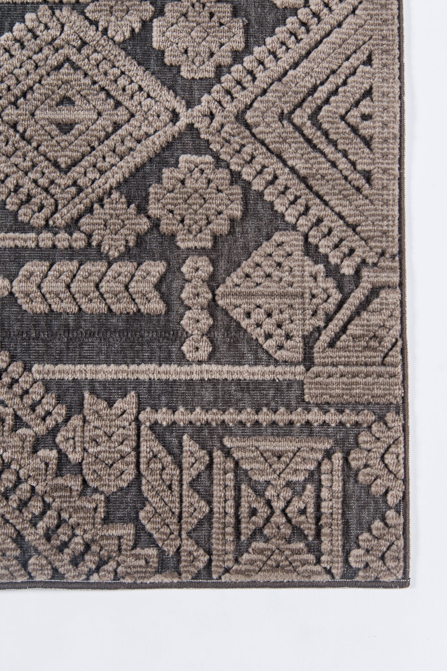 Geometric tribal rug corner in taupe and brown, woven with diamond and floral motifs.