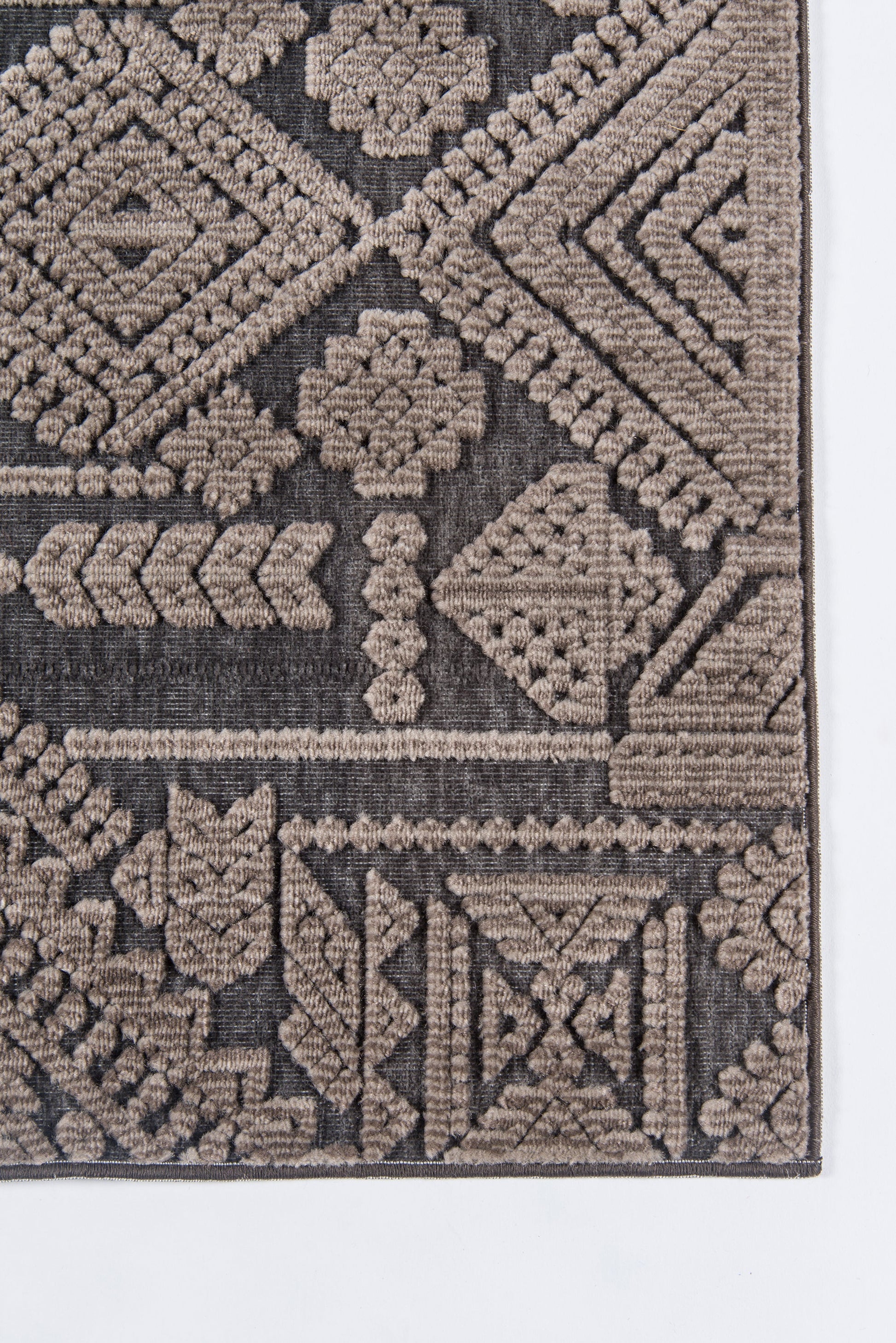 Geometric tribal rug corner in taupe and brown, woven with diamond and floral motifs.