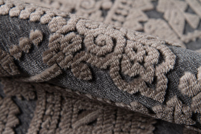 Close-up of tan embroidered floral damask pattern on charcoal gray woven rug.