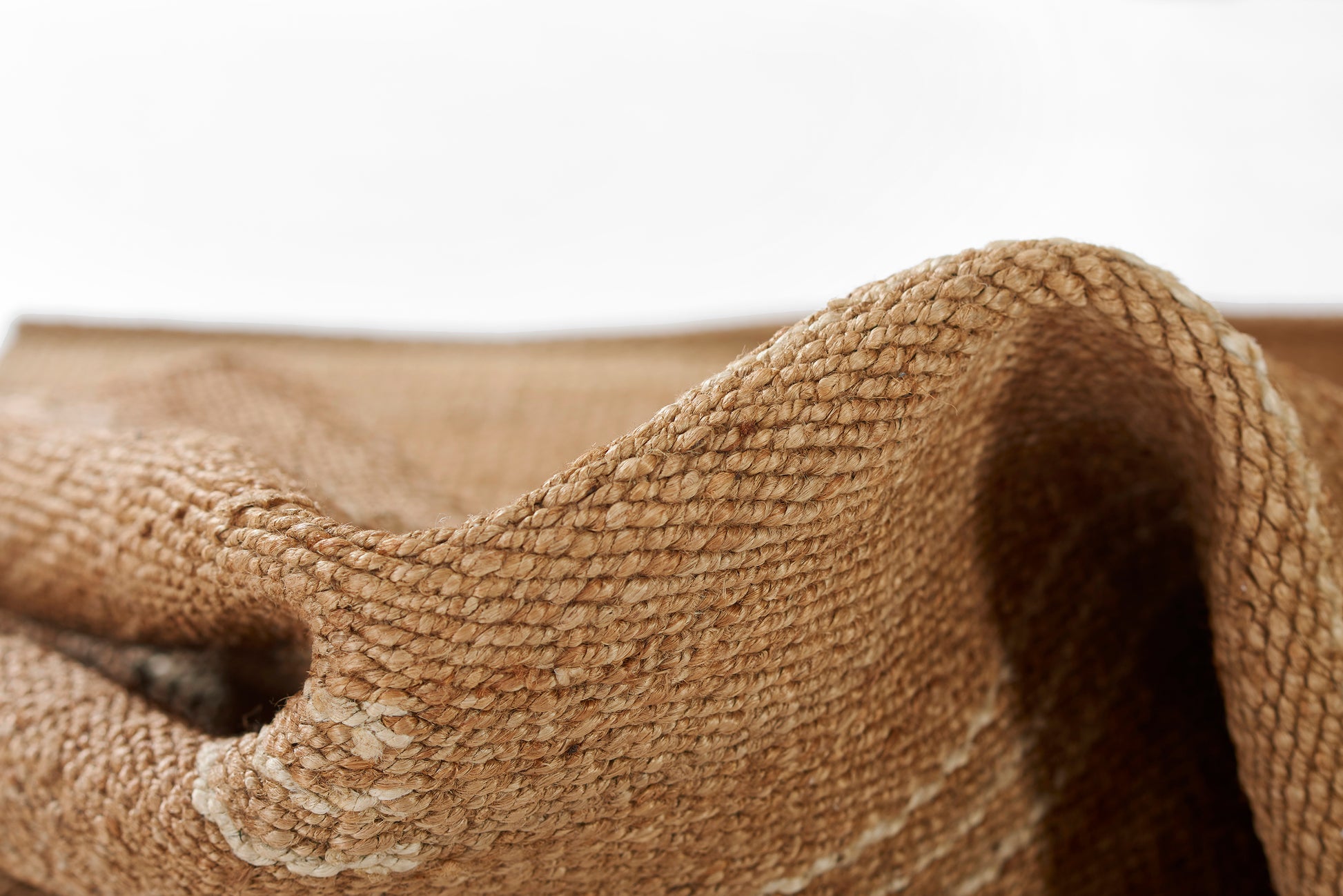 Natural beige woven jute rug close-up with textured folds, rustic handmade style.