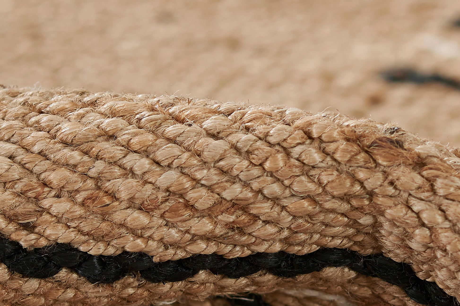 Close-up of a natural jute rug with a black stripe and beige braided texture for rustic coastal decor