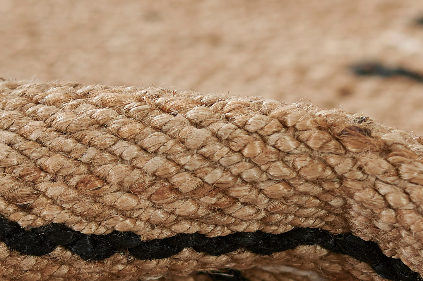 Close-up of a rug with a broken stripe pattern in natural tones, including a black stripe, showing woven fibers.