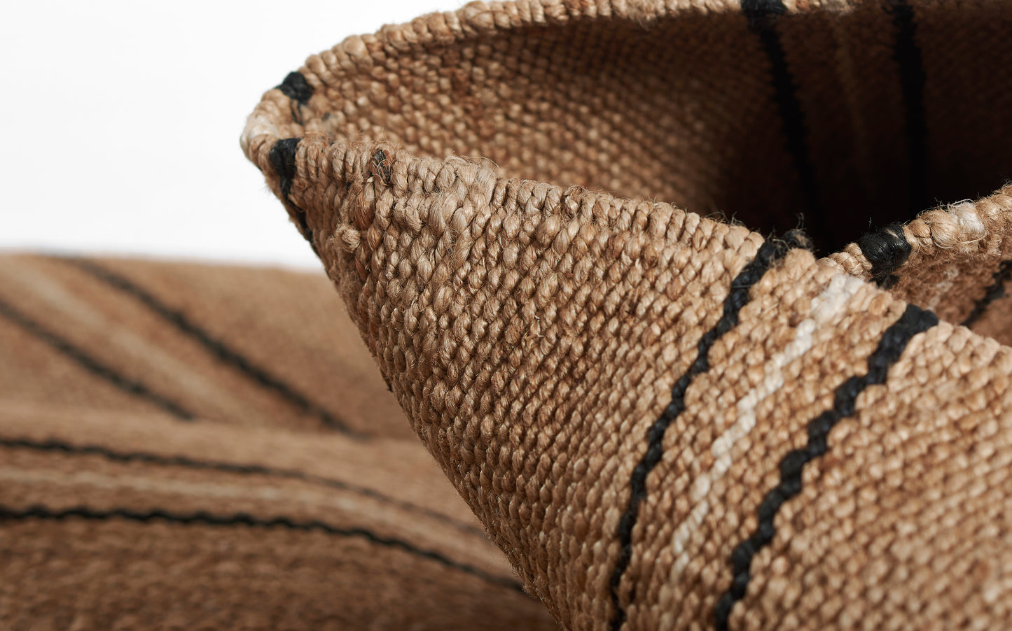 Natural tan woven rug with black stripes; thick textured jute fabric with a folded edge.