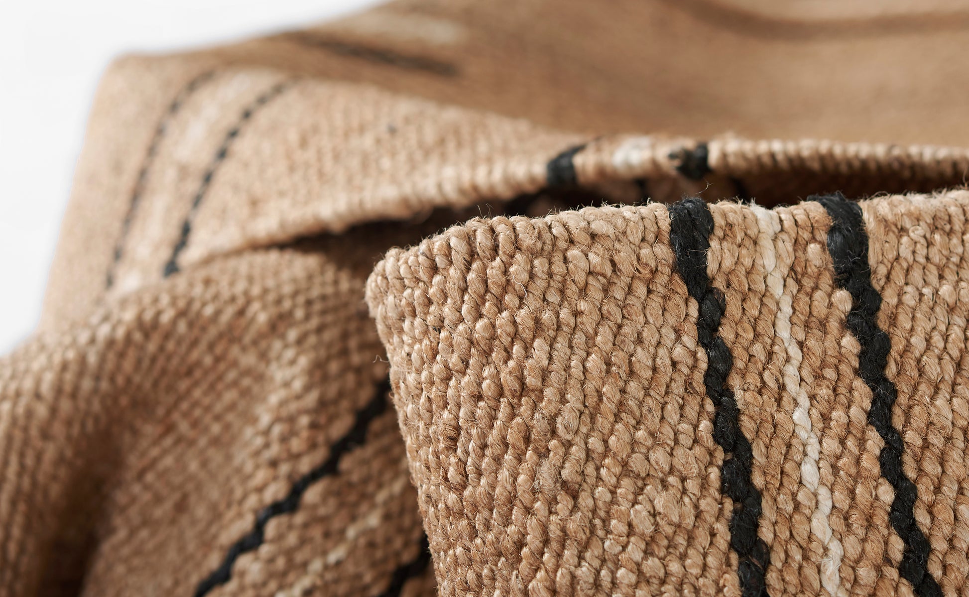 Close-up of natural beige woven textile with dark stripes; thick textured fibers, folded like a throw blanket.