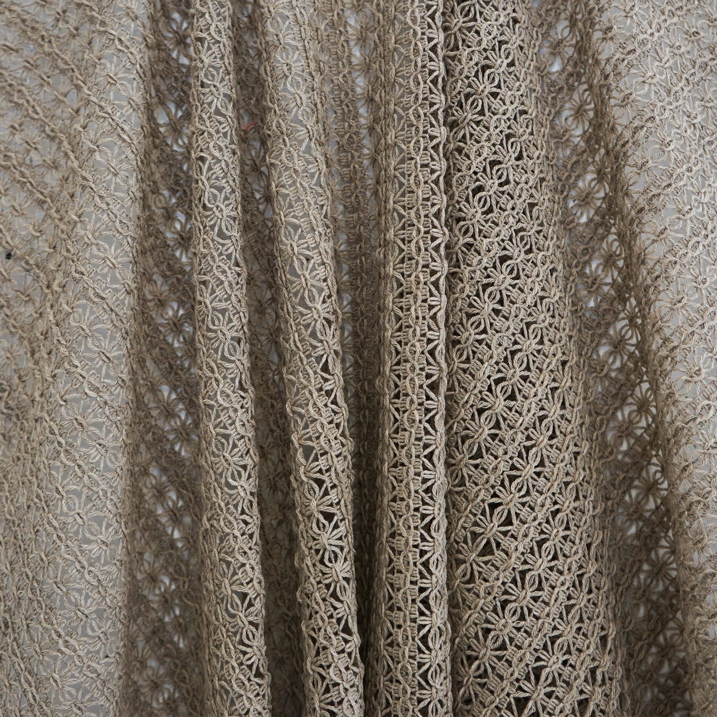 Beige crochet lace fabric with open floral lattice pattern and soft drape, ideal for shawls or lightweight garments.