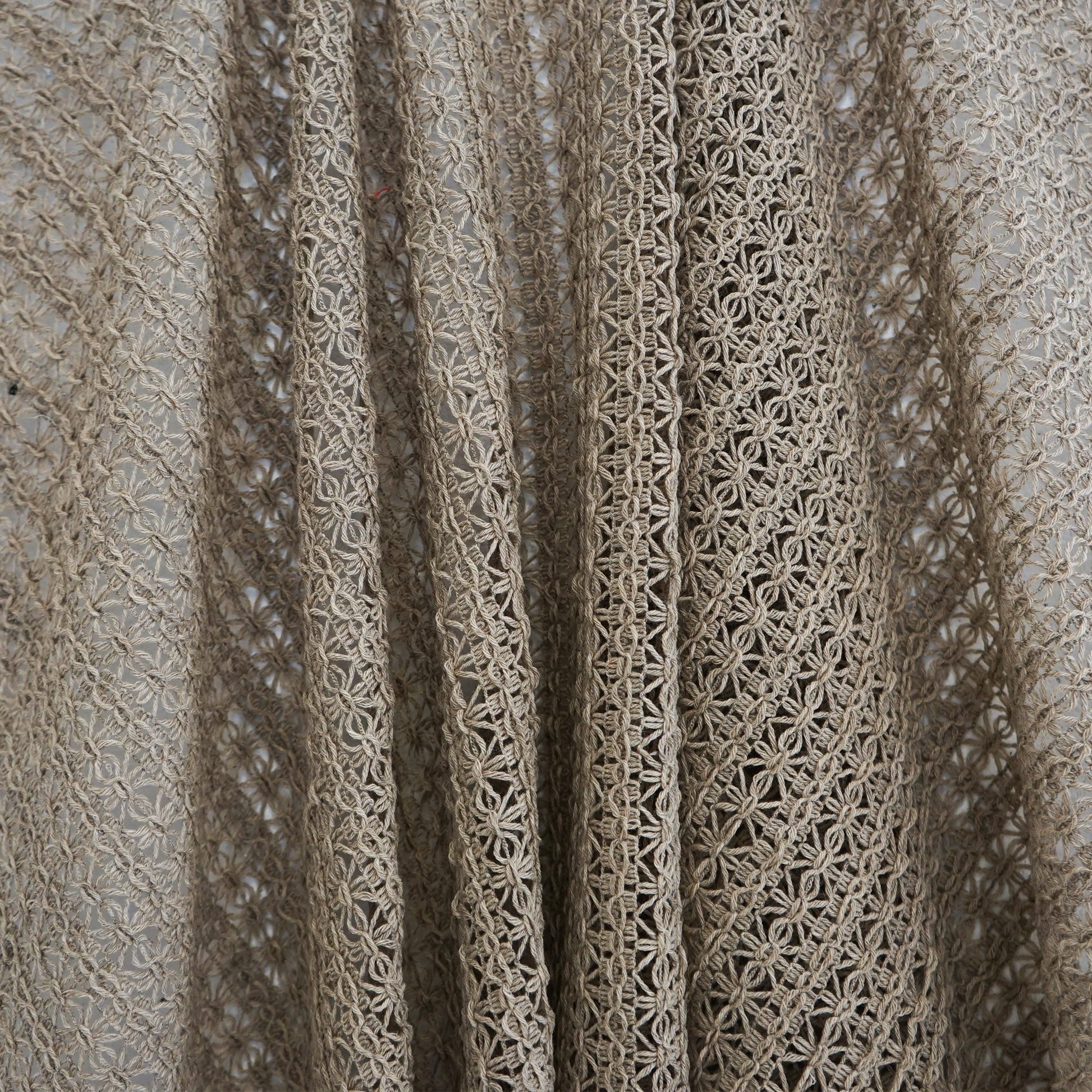 Beige crochet lace fabric with open floral lattice pattern and soft drape, ideal for shawls or lightweight garments.