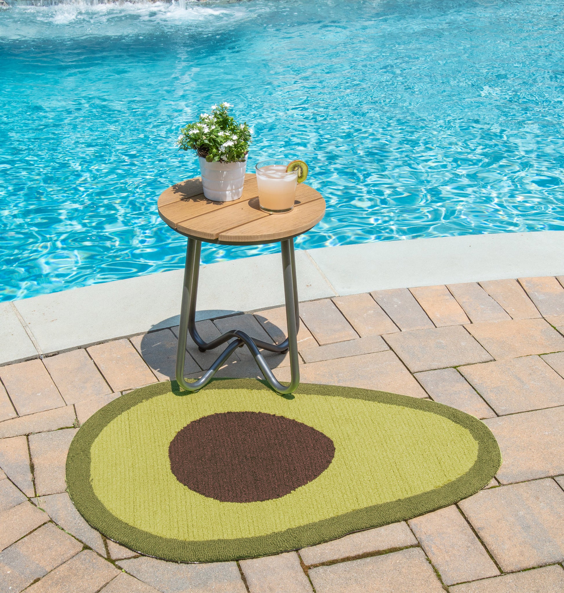 Lime-green outdoor rug beside the pool; poolside scene with a round wooden-top table, plant pot and lemonade.