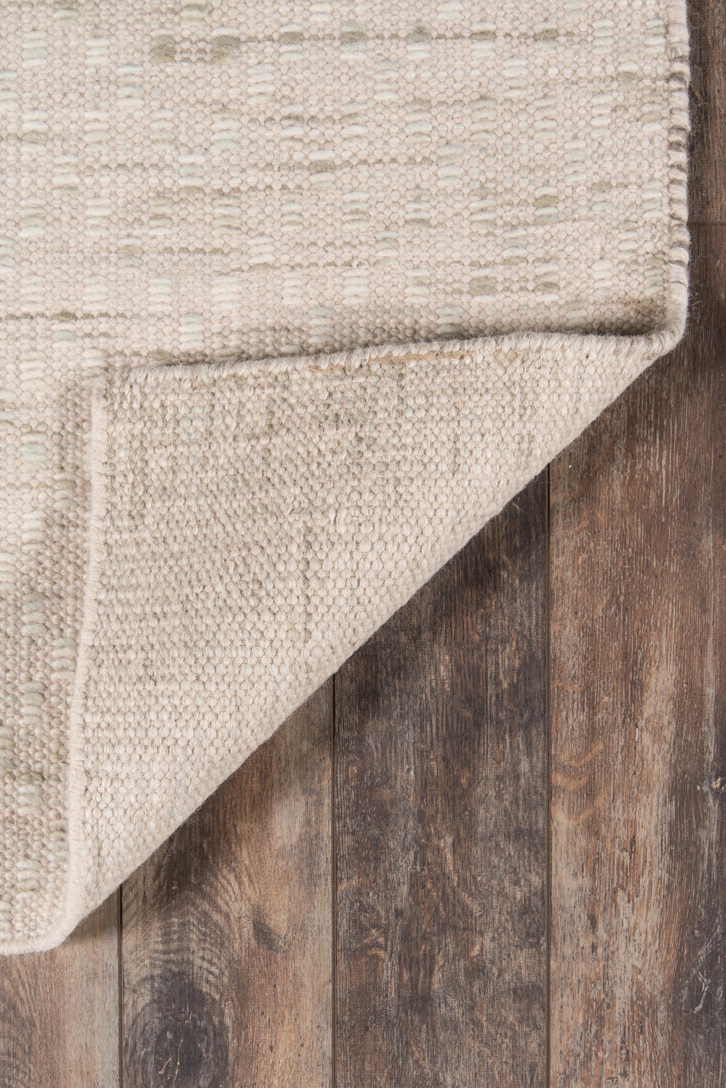 Beige woven rug corner folded over dark wooden floor; natural fiber texture, rustic & chic rug.