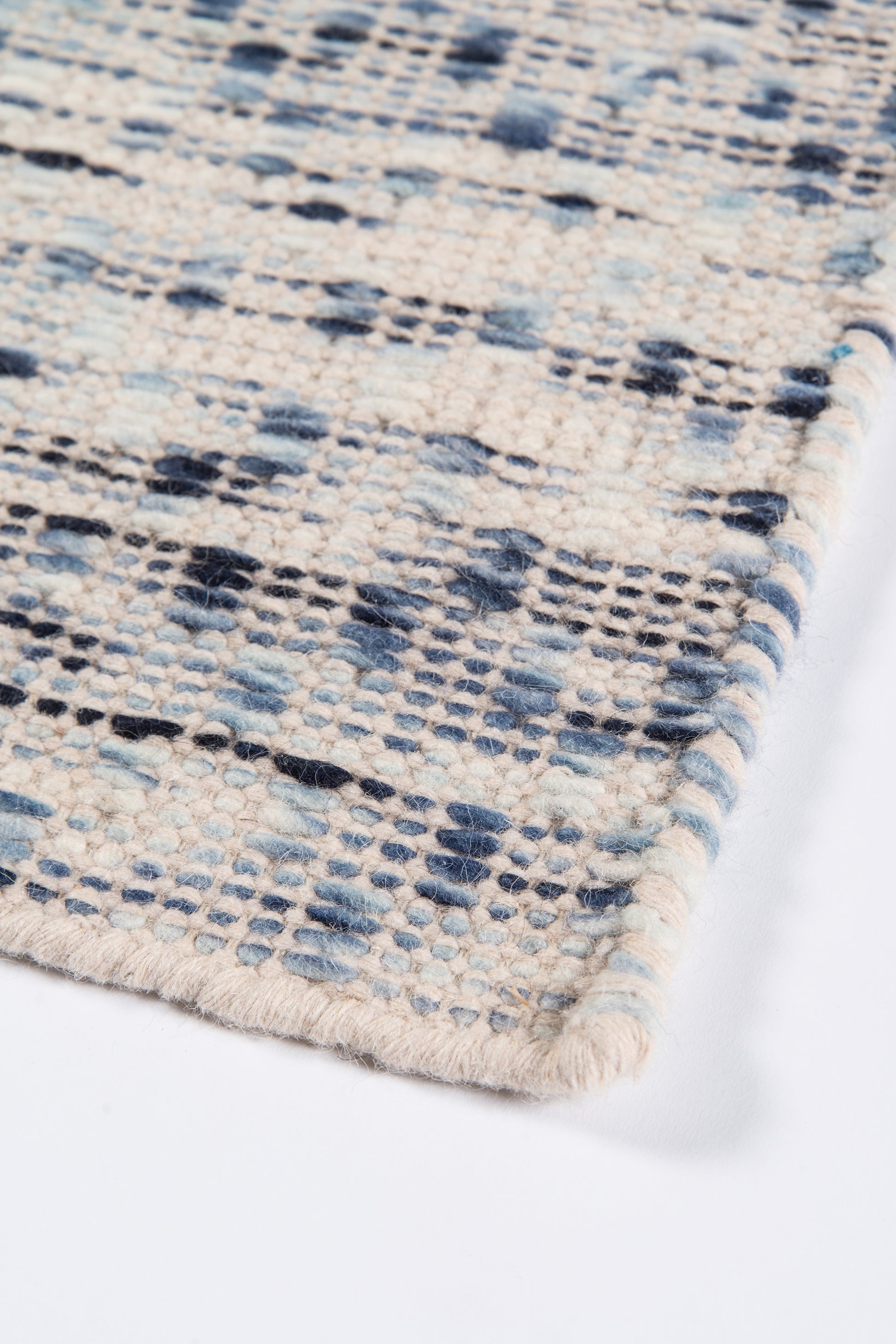 Close-up of a cream woven rug with blue and navy geometric pattern and fringed edge.