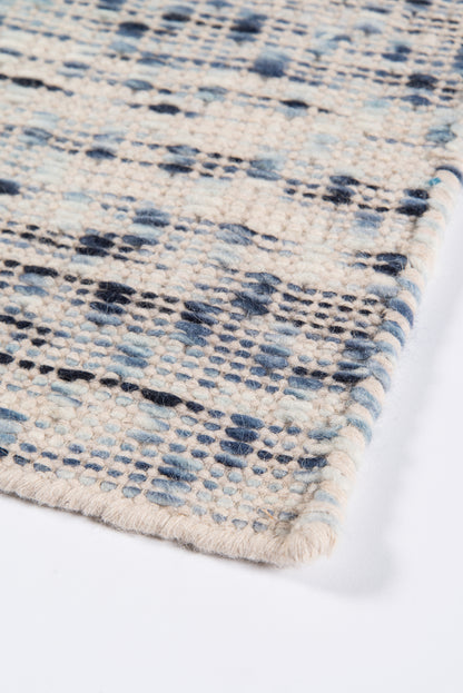 Close-up of a cream woven rug with blue and navy geometric pattern and fringed edge.