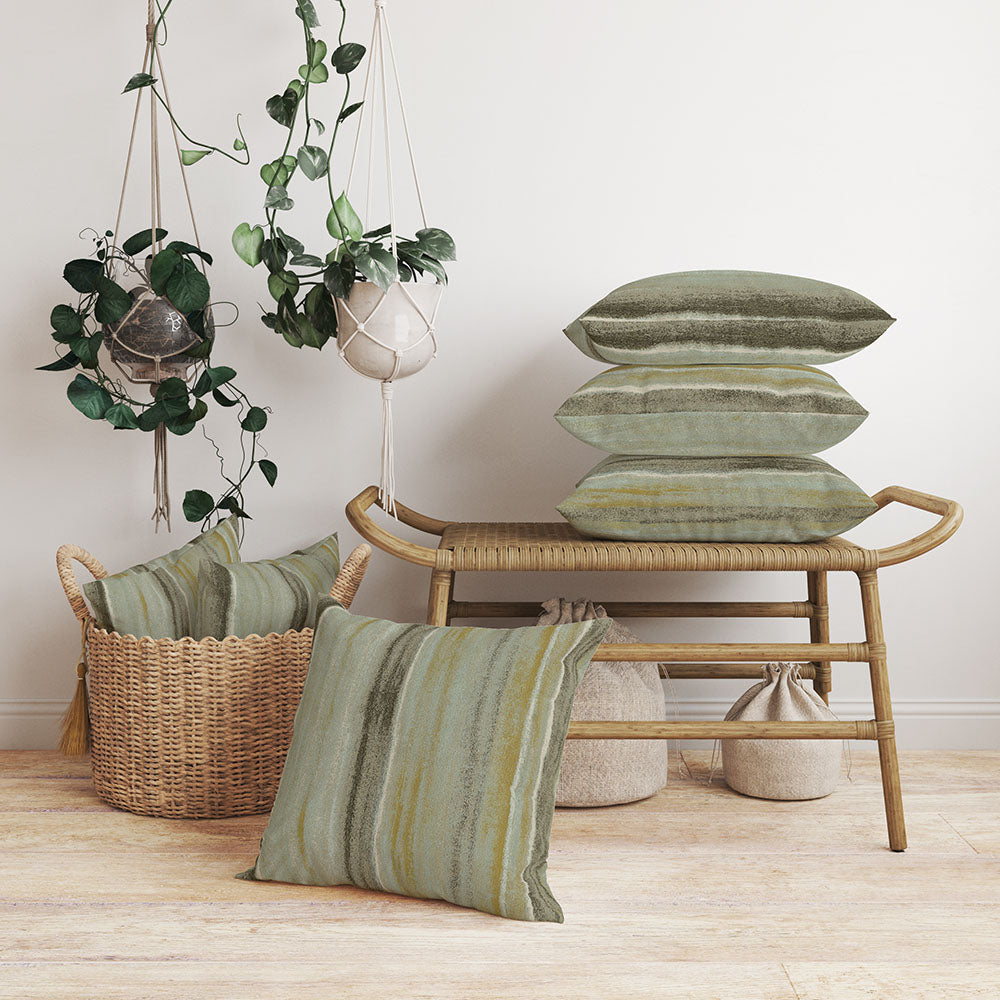 Olive-green striped cushions on a natural rattan bench, with hanging macrame planters and a woven basket of extra pillows.