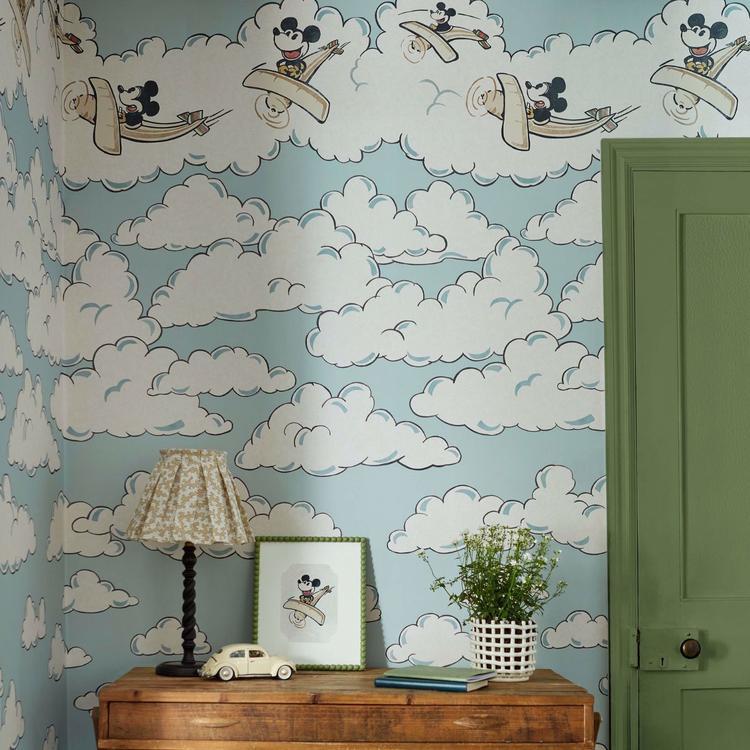 Disney Home x Sanderson Mickey in the Clouds wallpaper mural featuring Mickey Mouse flying through soft pastel clouds and airplanes in a whimsical vintage sky design. Classic Disney nursery wallpaper ideal for kids bedrooms, playrooms, and Disney themed interiors. Dreamy cloud wallpaper mural perfect for nursery décor, feature walls, children’s room design, and vintage Disney home styling.