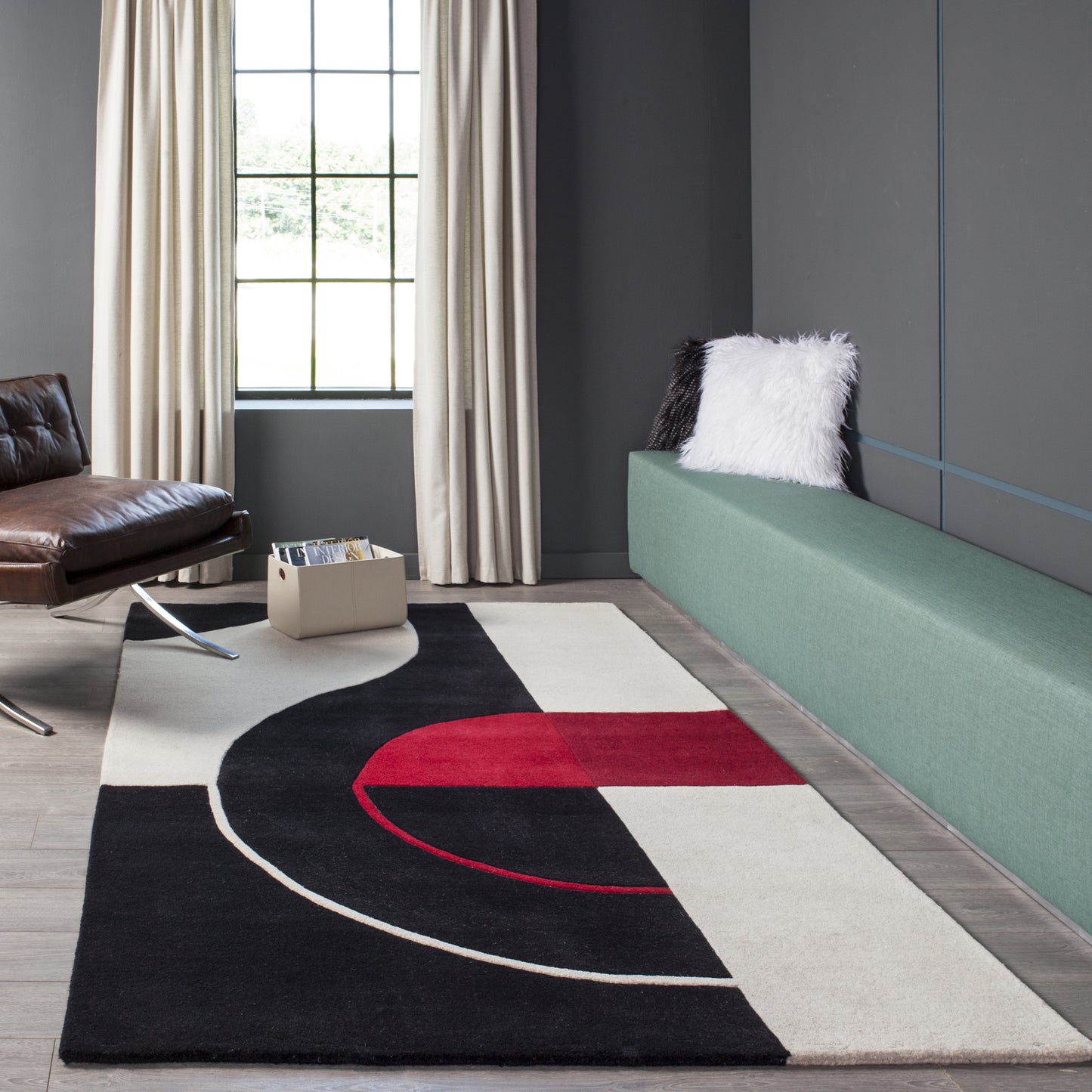 Geometric rug in black, cream and red with curved arc design on a dark floor beside a green banquette.