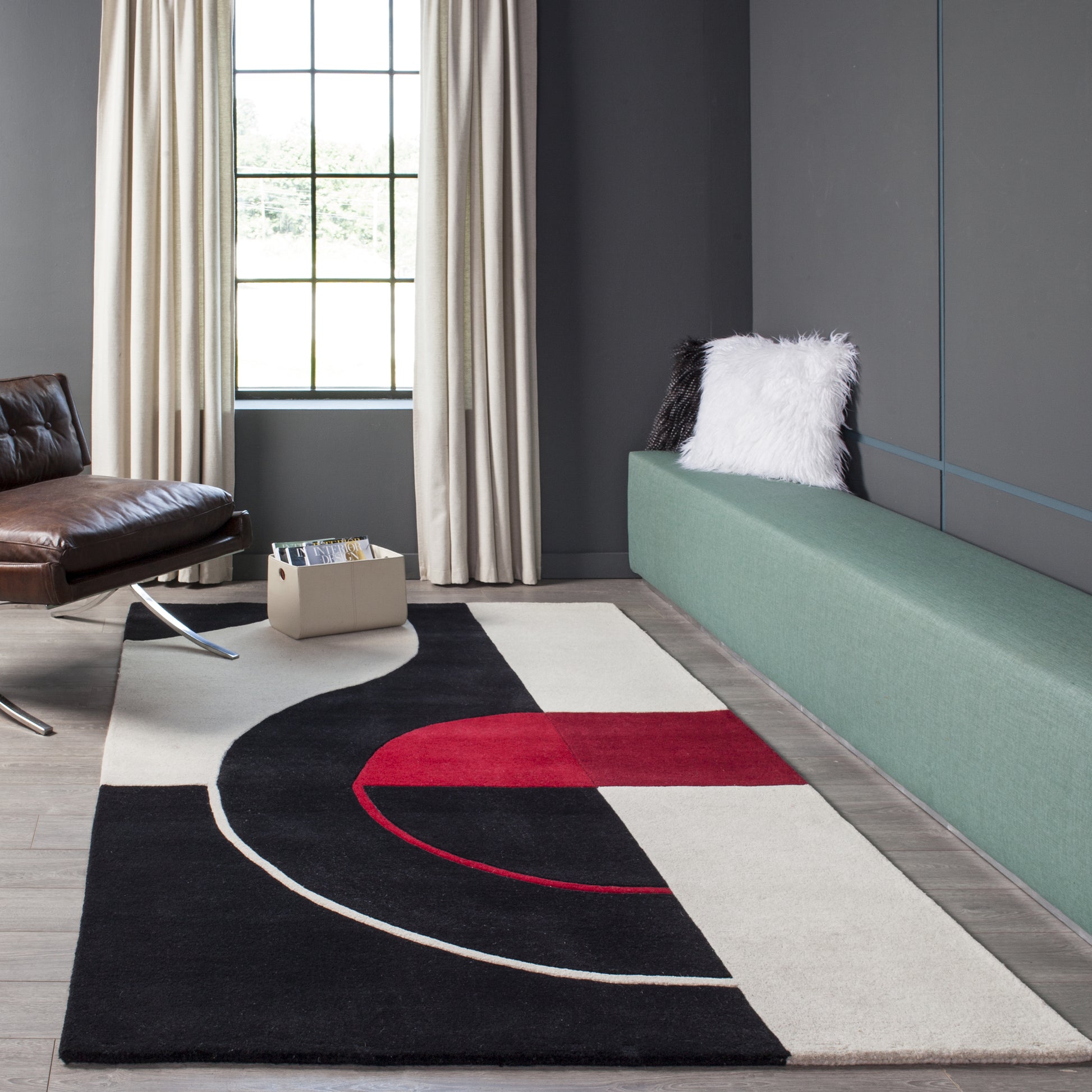 Geometric rug in black, cream and red with curved arc design on a dark floor beside a green banquette.