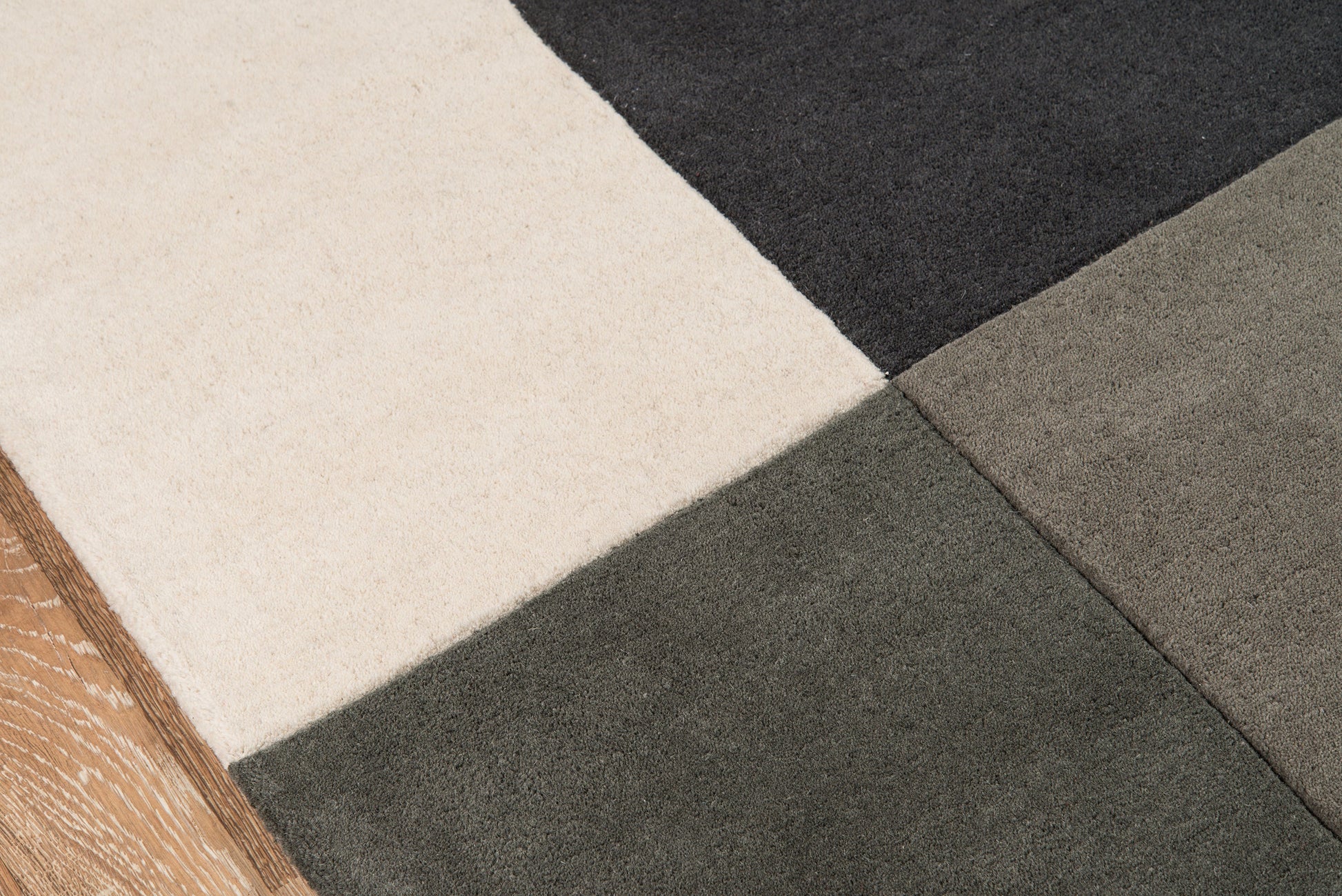 Patchwork rug in cream, beige, taupe and charcoal with diagonal seams; modern geometric floor decor.