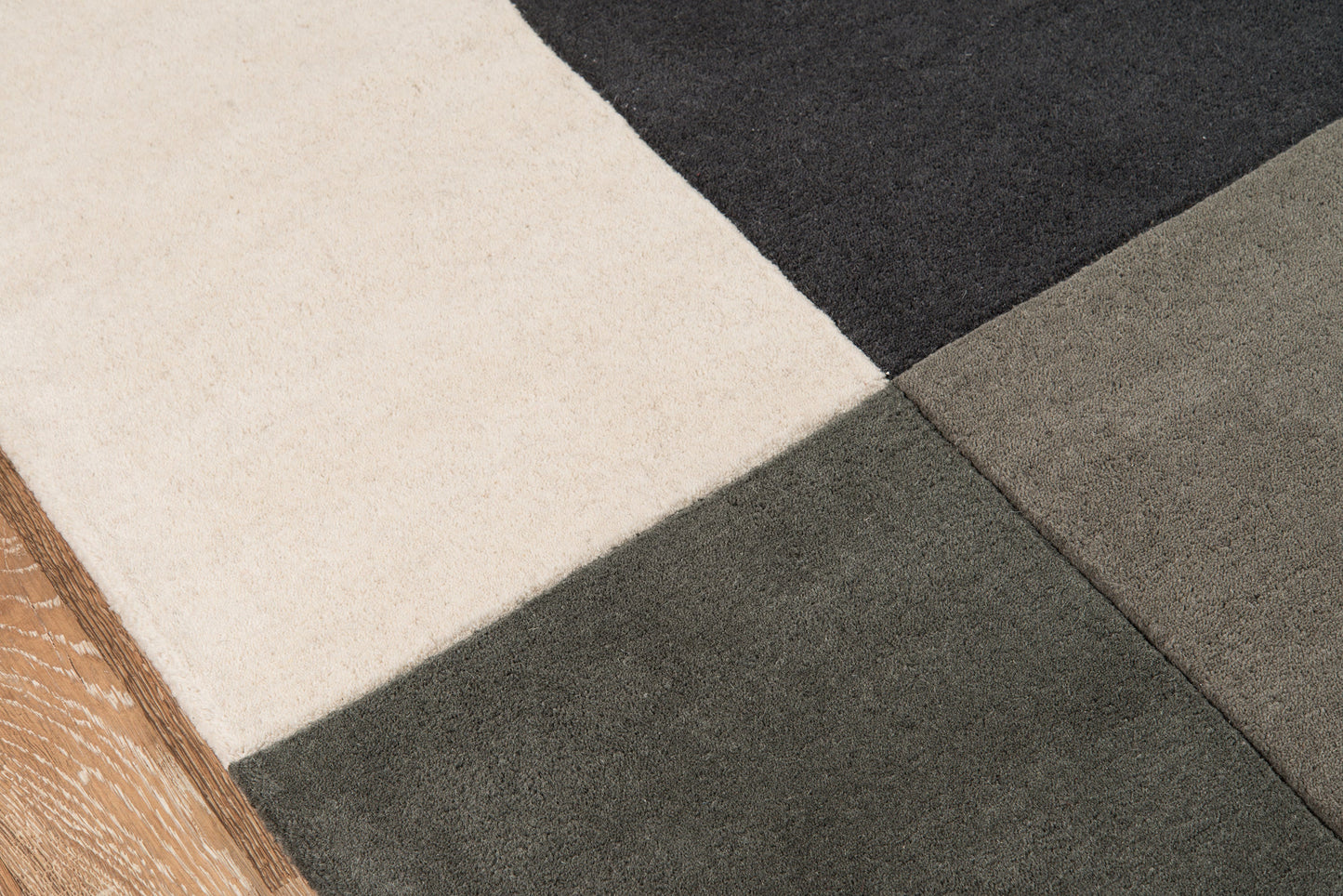 Close-up of a cream, gray, taupe & charcoal area rug with a wooden edge on the left.