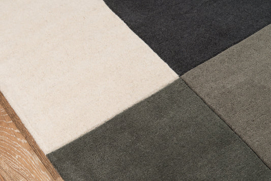 Close-up of a cream, gray, taupe & charcoal area rug with a wooden edge on the left.