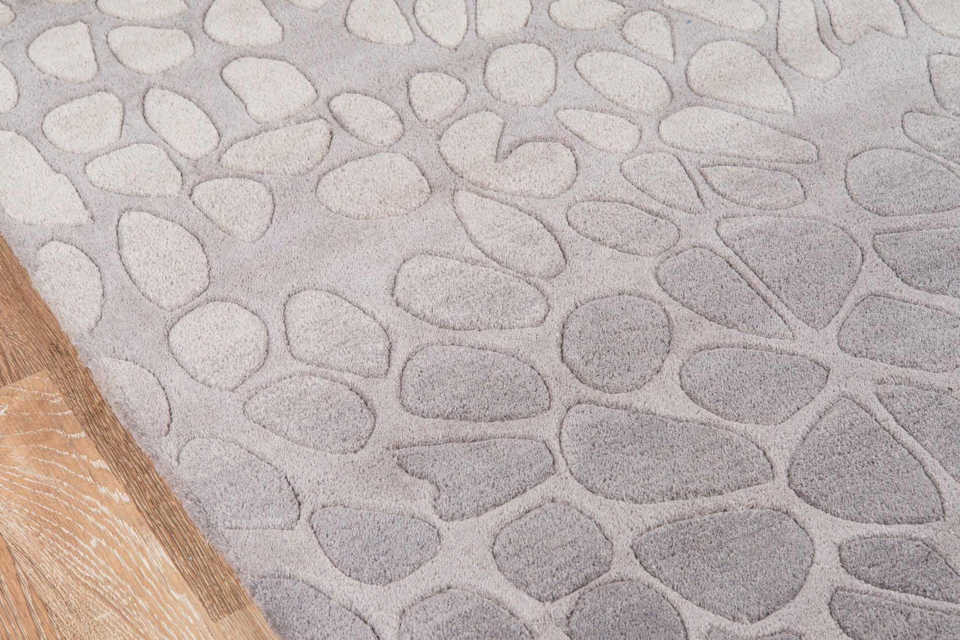 Gray pebble-pattern rug with irregular stone shapes; wooden floor edge visible