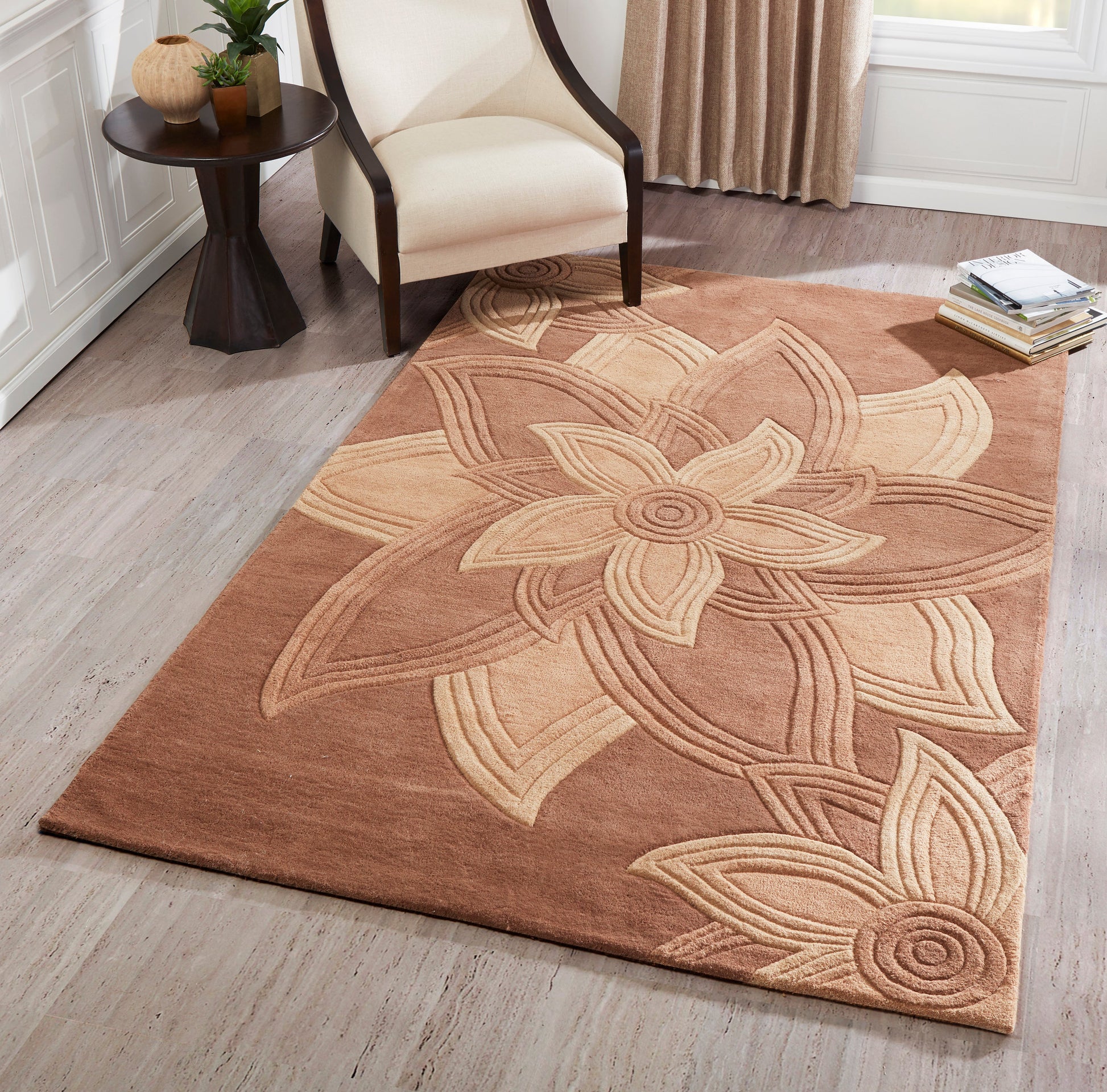 Warm brown area rug with a large beige floral motif in a cozy living room by a cream armchair and side table.